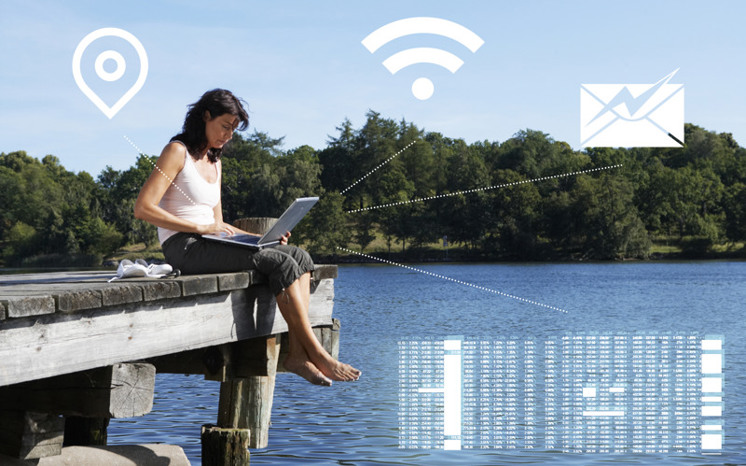 Digitala symboler över kvinna som sitter på en brygga och använder en bärbar dator.